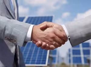 Two businessmen shake hands over solar panels